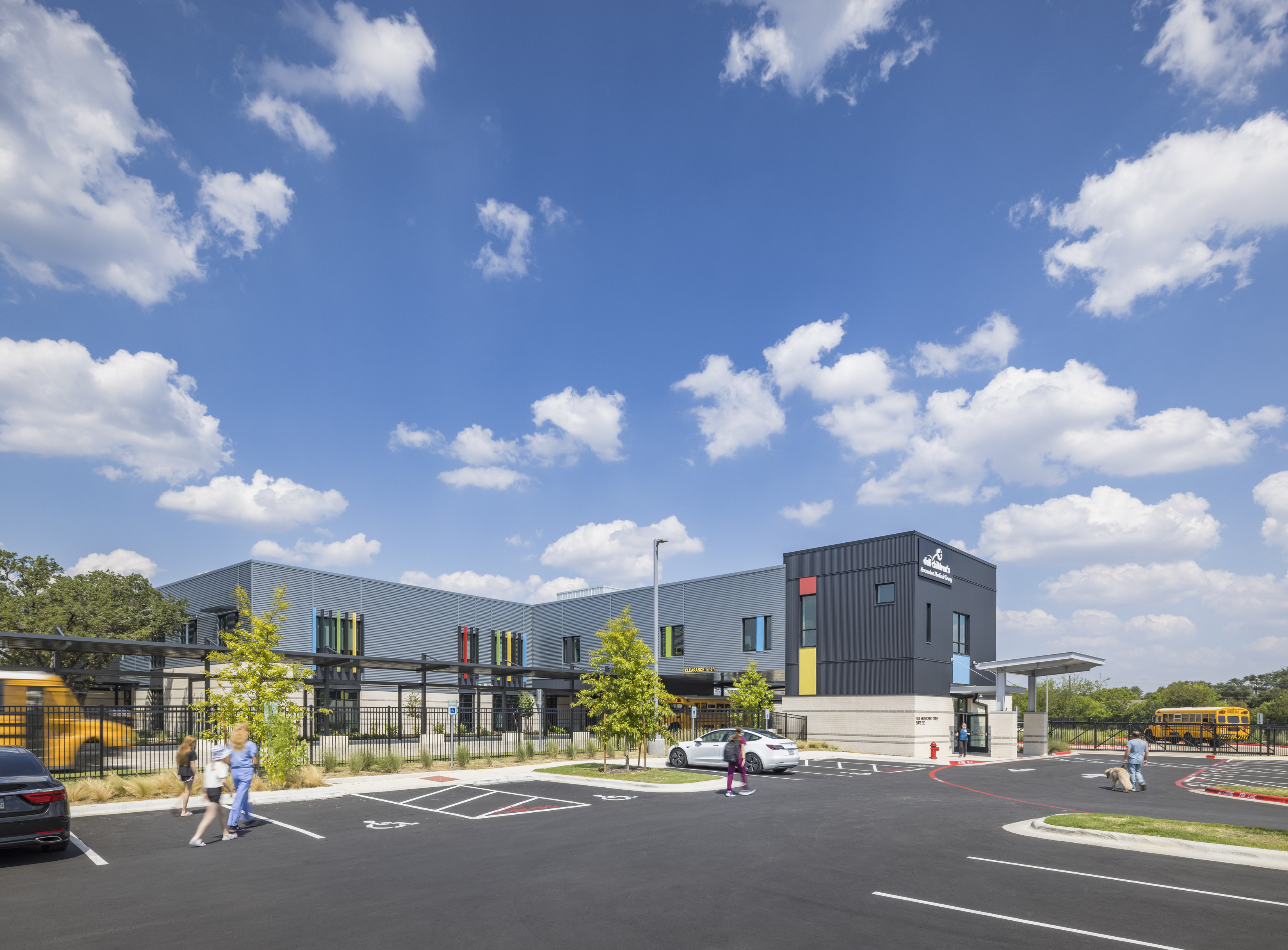 The exterior of The Rosedale School. A building with a modern design, featuring colorful windows and a parking area with students and buses nearby. 