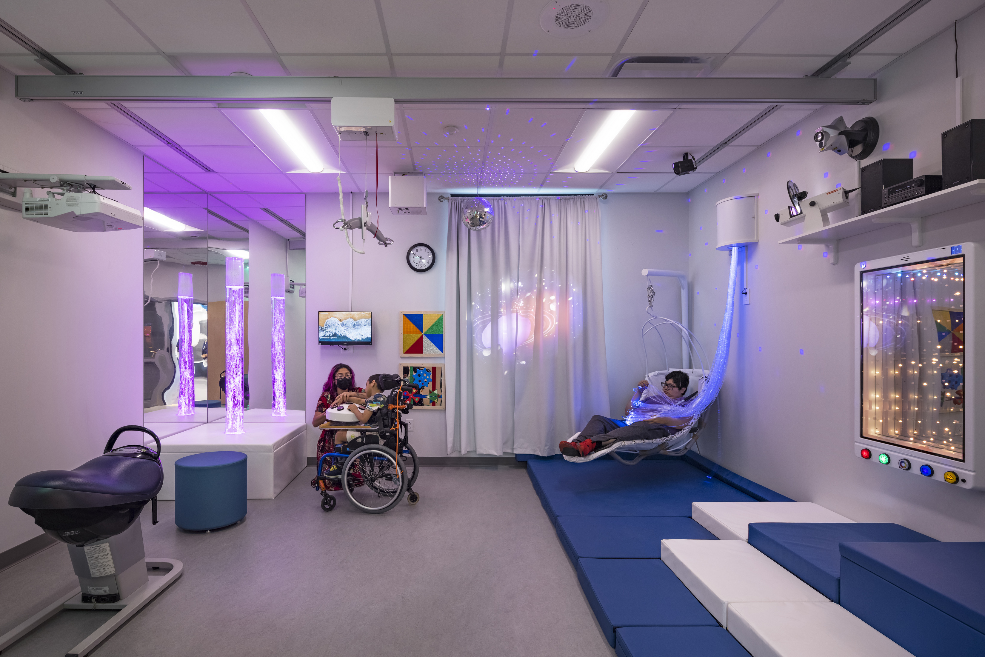 A sensory room with various interactive elements, including bubble tubes, a swing, and soft mats, designed for children with special needs. 