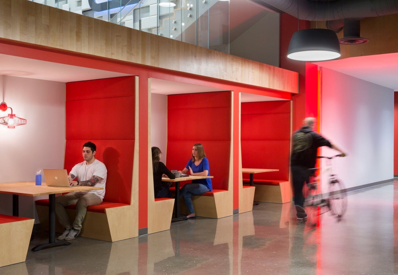 People sitting in booths in an office space and a person strolling by on a bicycle.